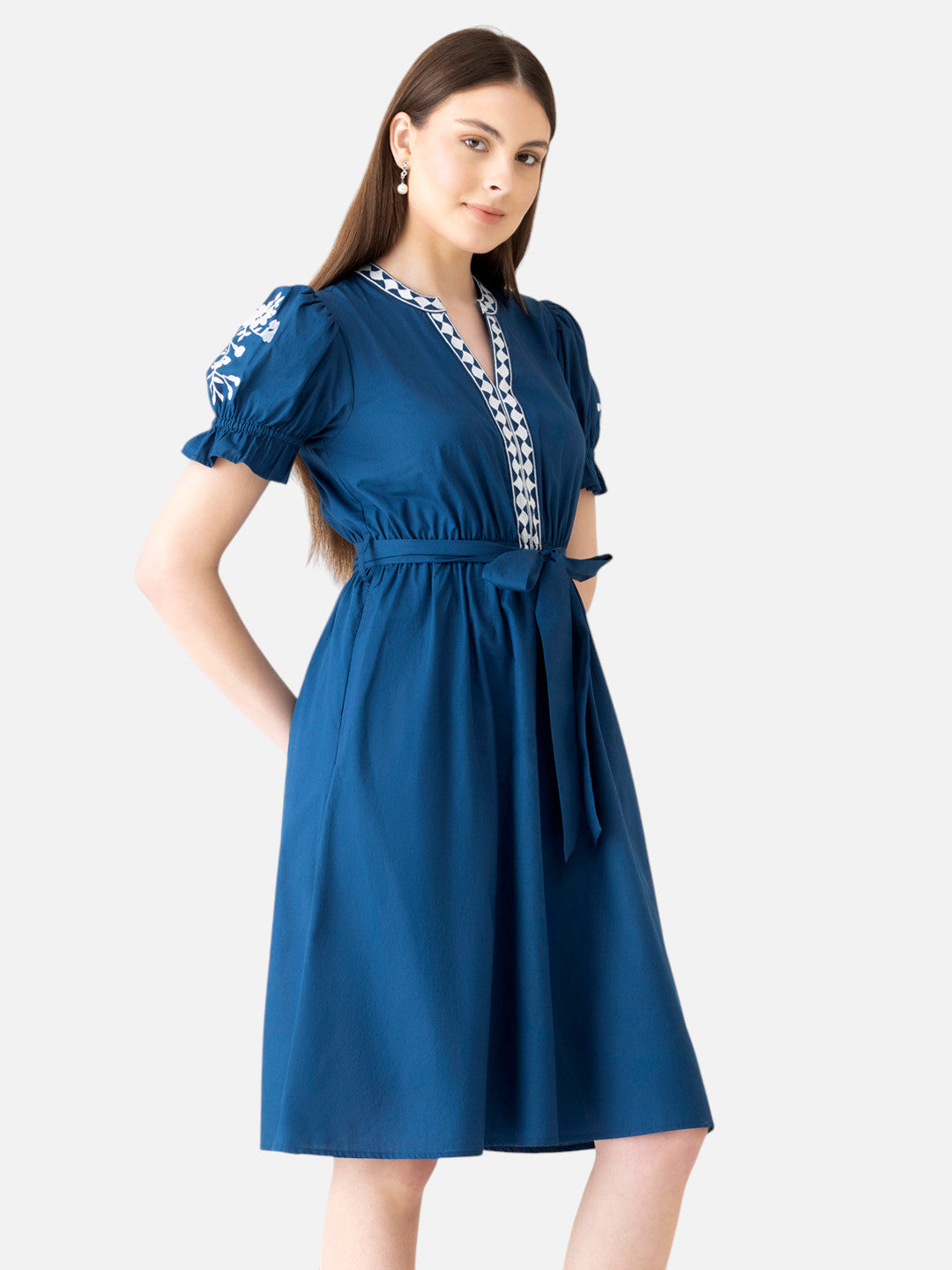 Woman wearing a blue knee-length dress with puff sleeves and white embroidered details