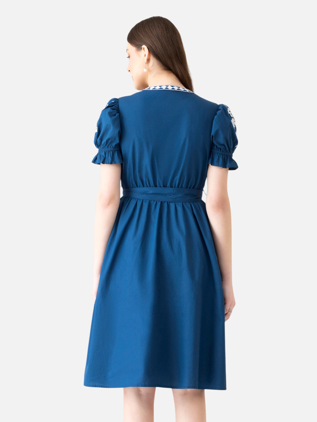 Woman in blue knee-length dress with short puff sleeves, belted waist, and embroidered collar, back view