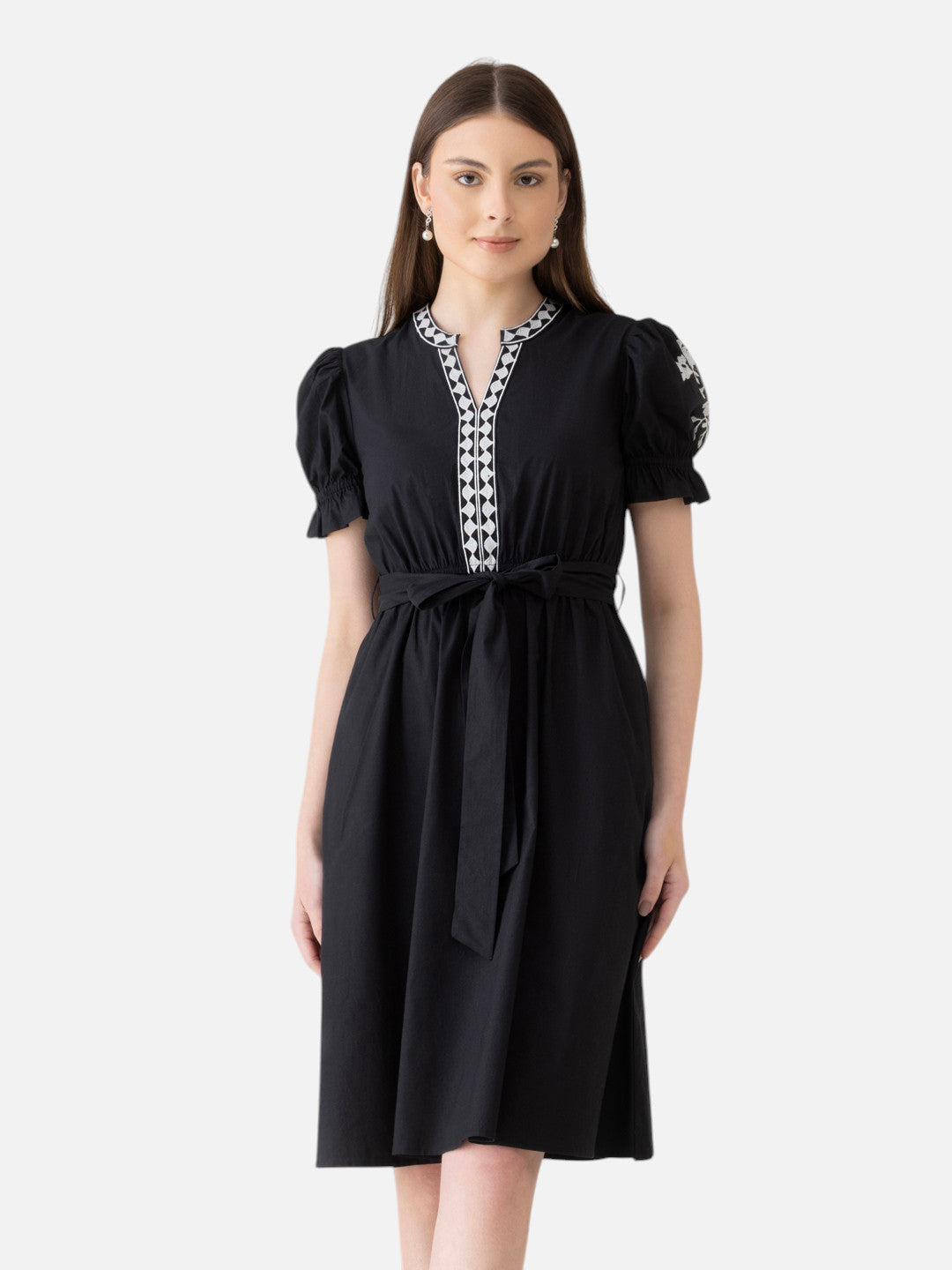 Woman wearing a black knee-length dress with puff sleeves, belt, and embroidered neckline