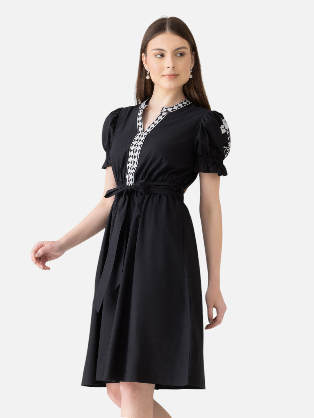 Woman wearing a black knee-length dress with white embroidered details and puff sleeves