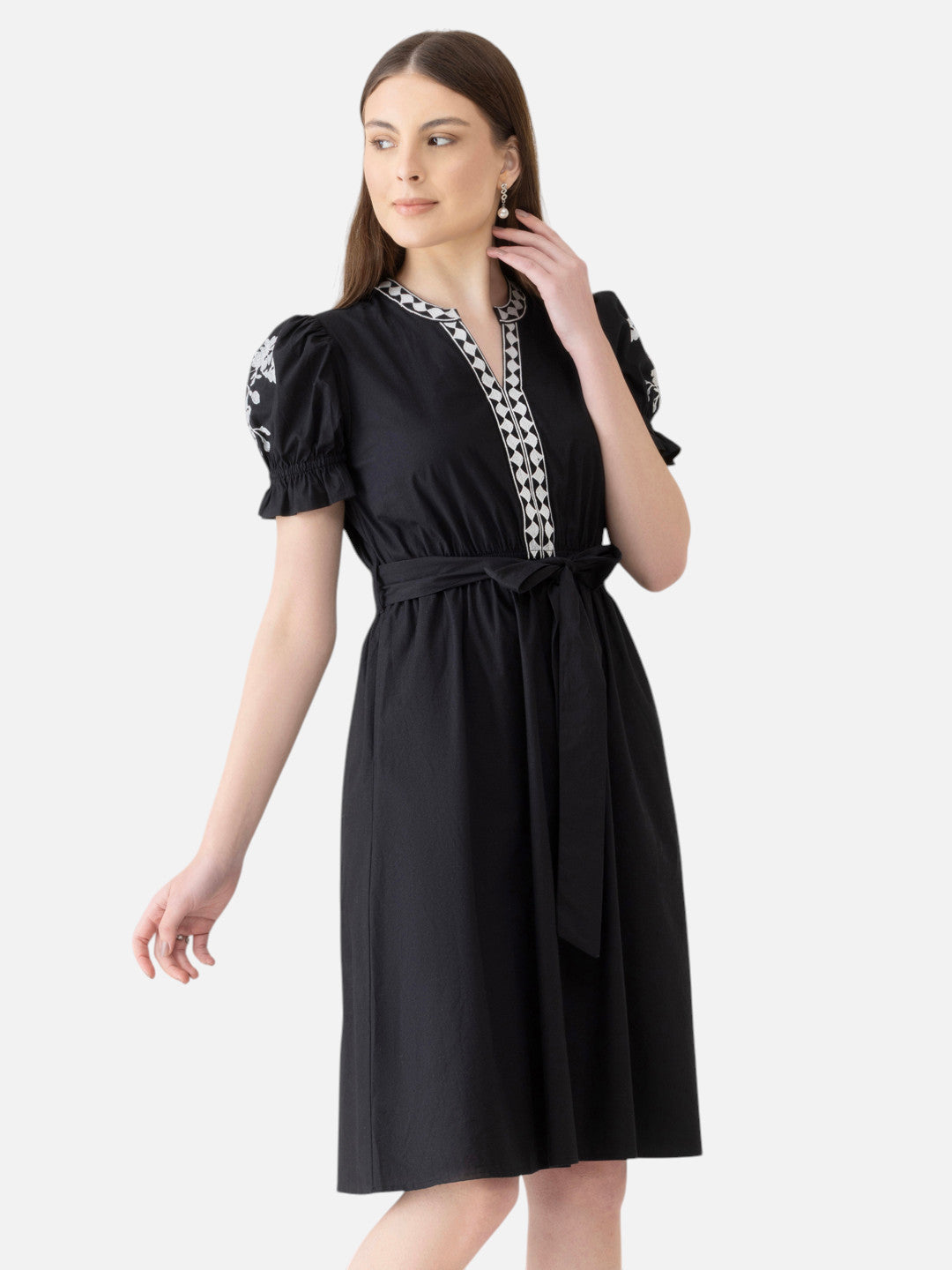 Woman wearing black knee-length dress with puff sleeves and geometric trim, belted waist
