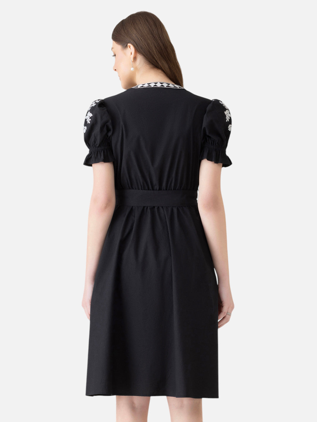 Back view of woman in knee-length black dress with puff sleeves and white floral embroidery