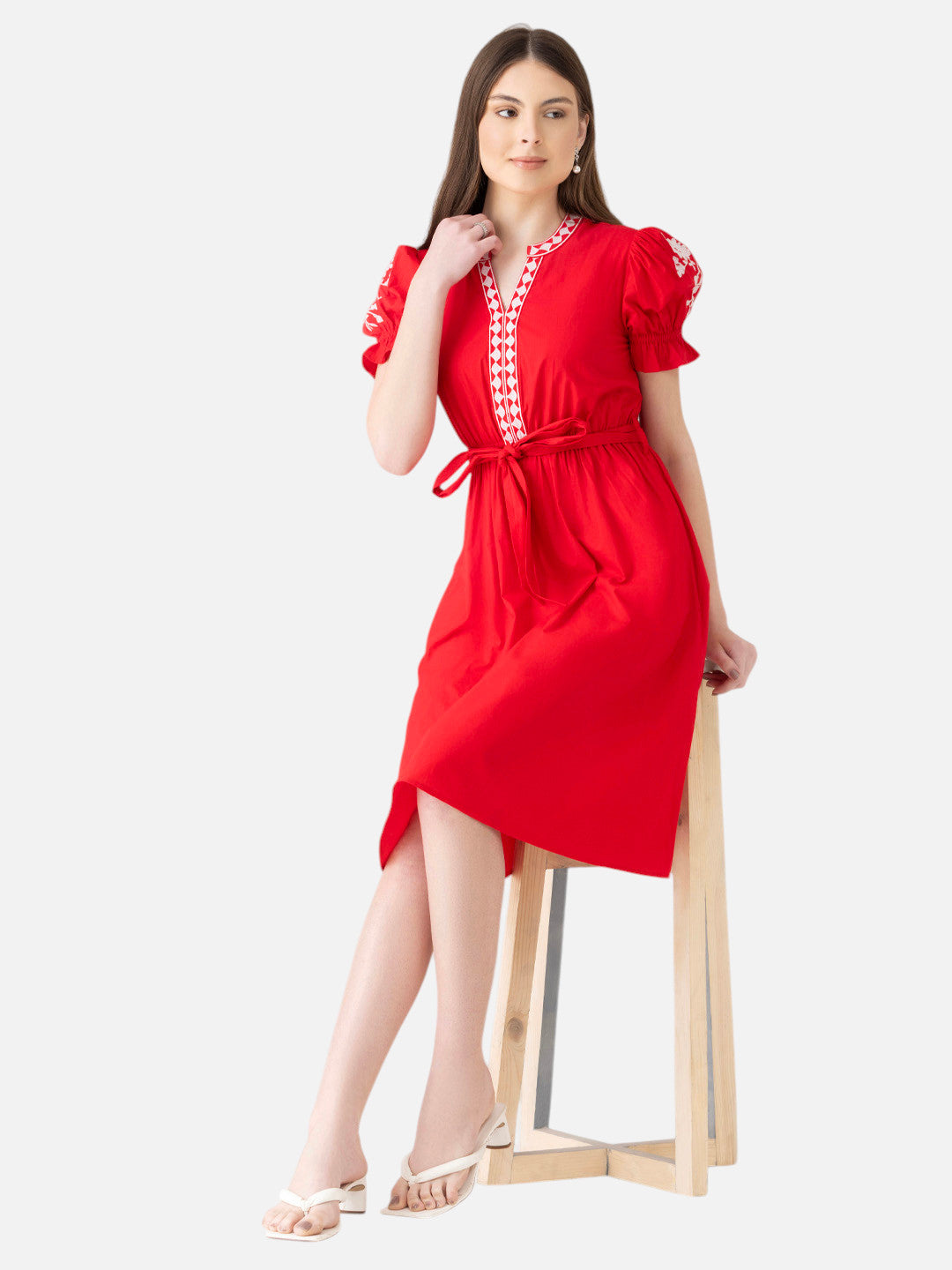 Woman in a red knee-length dress with embroidered trim and puff sleeves, sitting on a stool