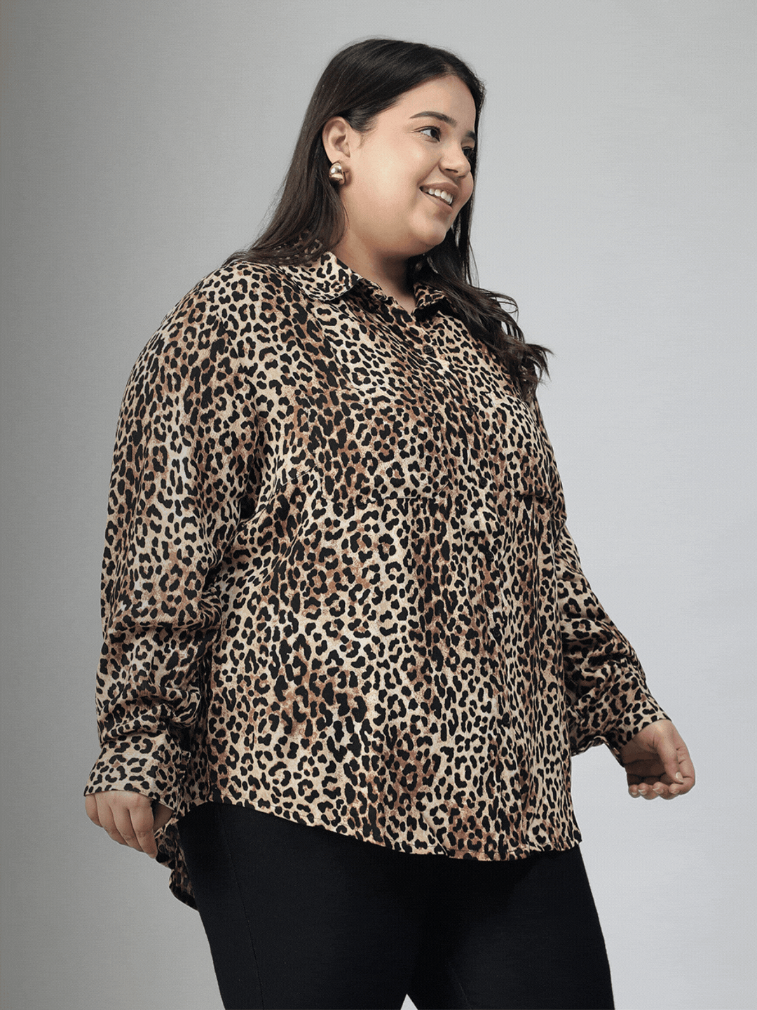 A woman with long dark hair is smiling and posing in a leopard print shirt.