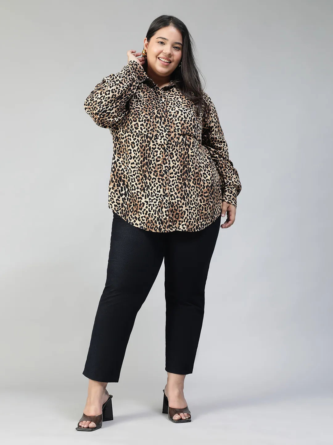 A woman with long dark hair is smiling and posing in a leopard print shirt.
