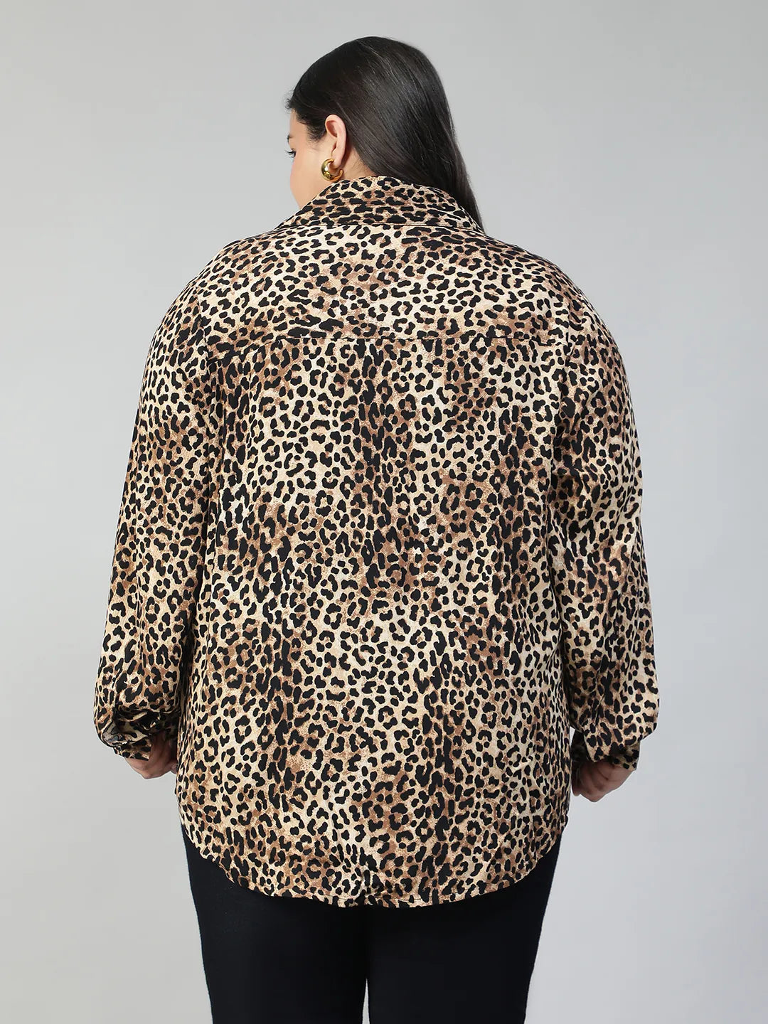 A woman with long dark hair is smiling and posing in a leopard print shirt.
