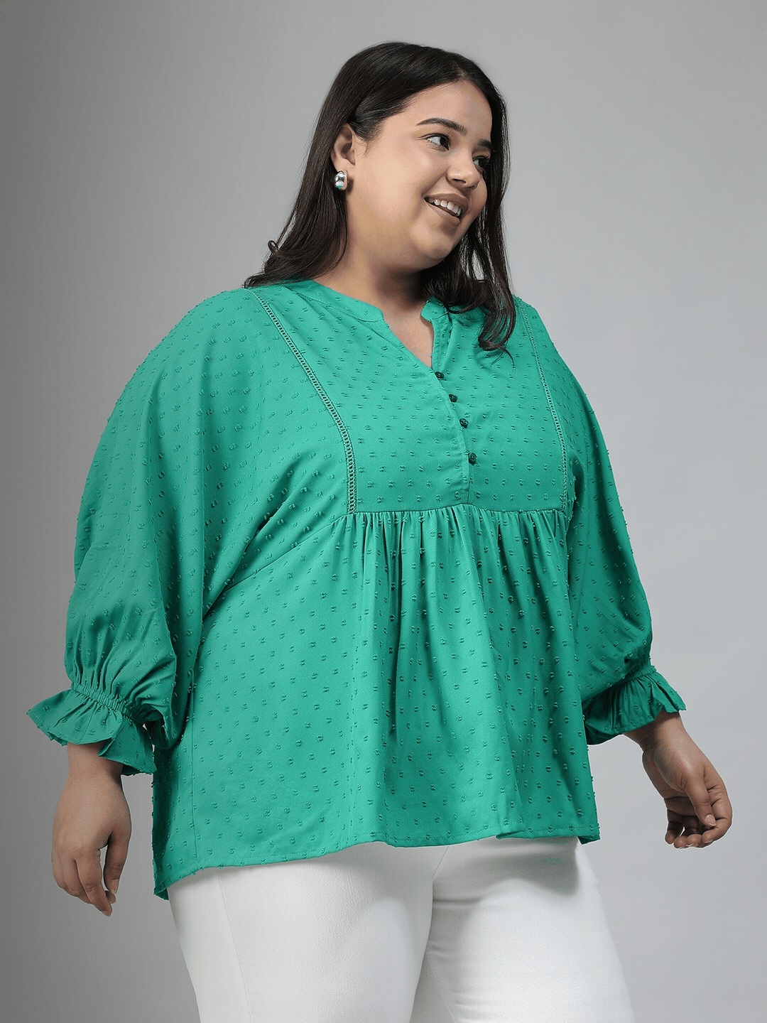 A smiling woman wearing a green blouse with a ruffled collar and buttons, posing for a photograph.