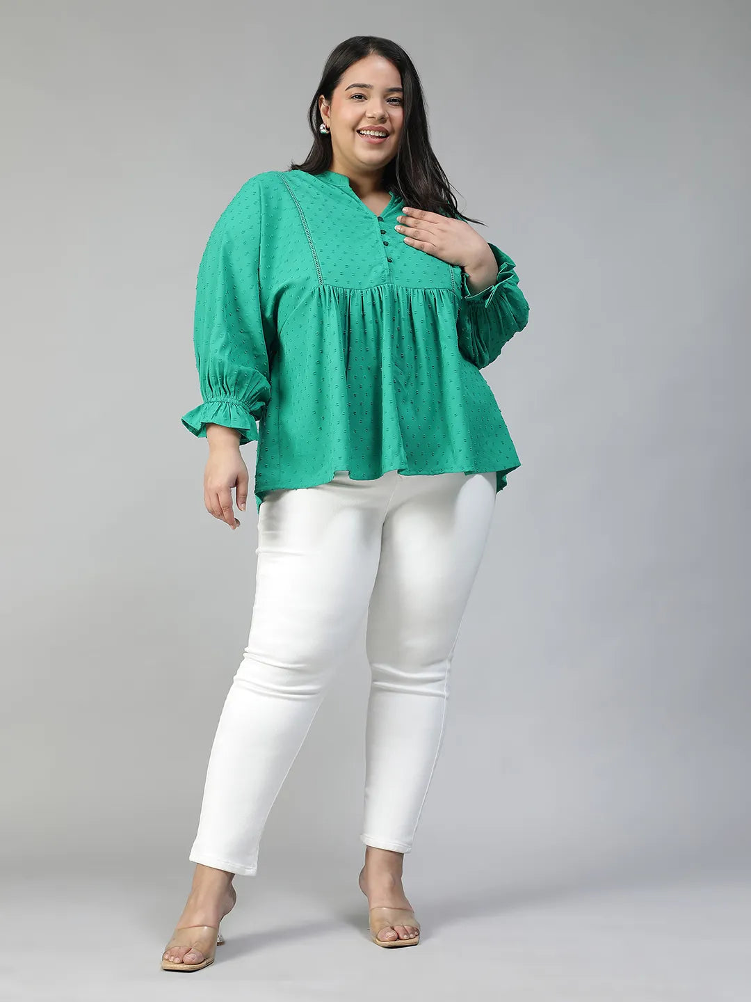 A smiling woman wearing a green blouse with a ruffled collar and buttons, posing for a photograph.
