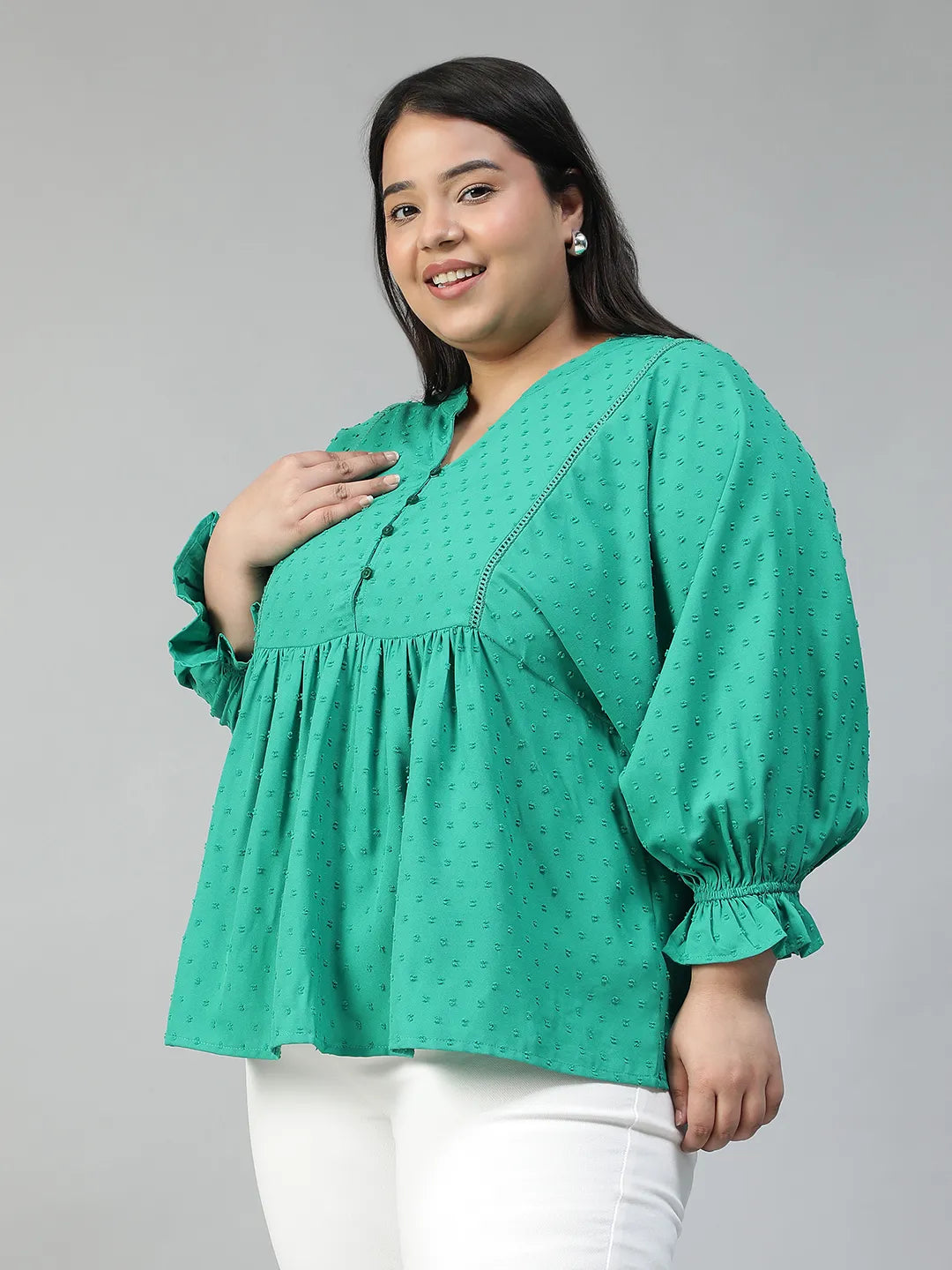 A smiling woman wearing a green blouse with a ruffled collar and buttons, posing for a photograph.