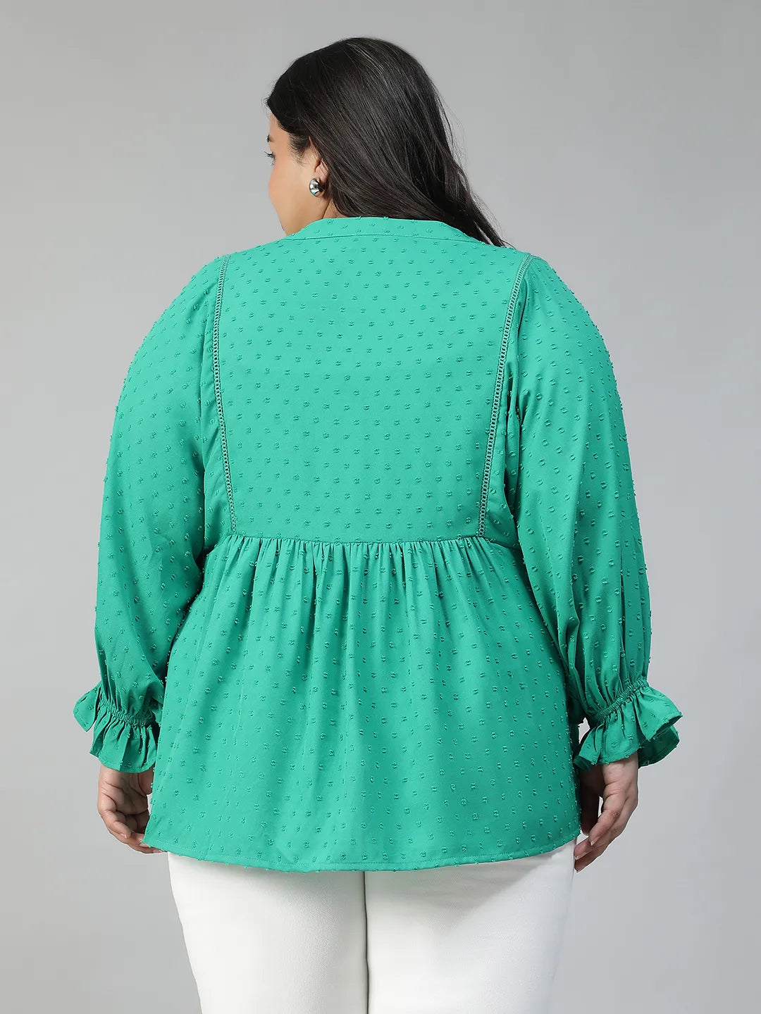 A smiling woman wearing a green blouse with a ruffled collar and buttons, posing for a photograph.