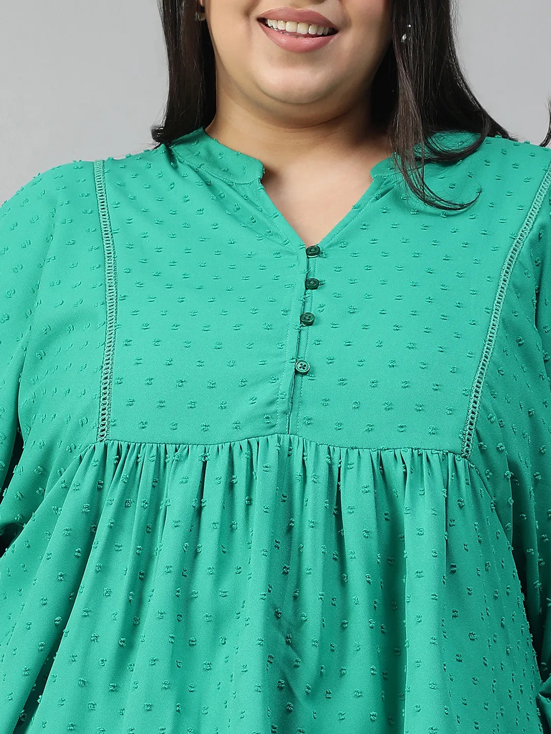 A smiling woman wearing a green blouse with a ruffled collar and buttons, posing for a photograph.