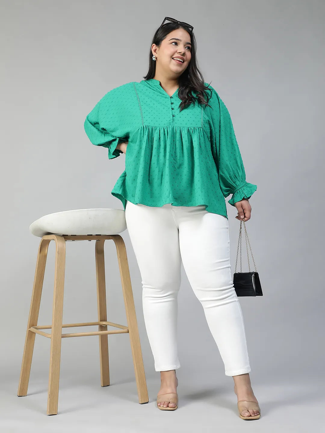 A smiling woman wearing a green blouse with a ruffled collar and buttons, posing for a photograph.