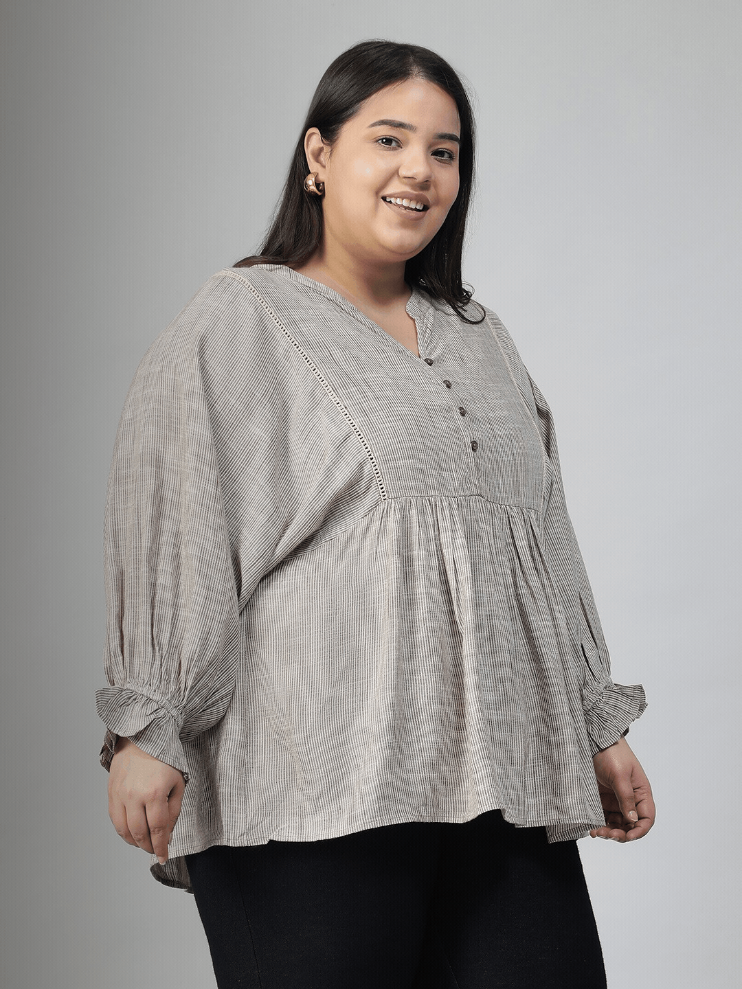 A woman with long dark hair is smiling and wearing a gray blouse with puffed sleeves.