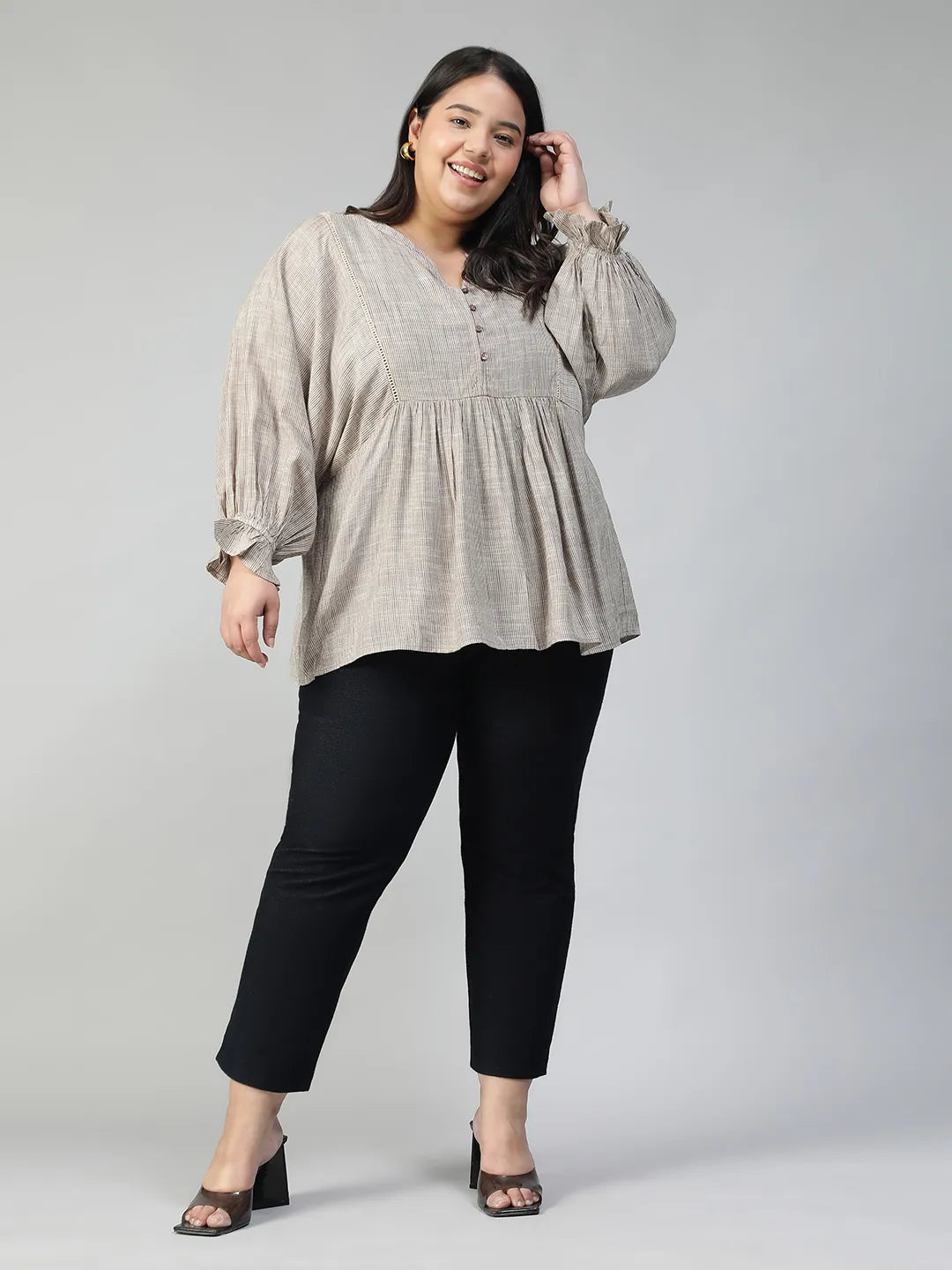A woman with long dark hair is smiling and wearing a gray blouse with puffed sleeves.