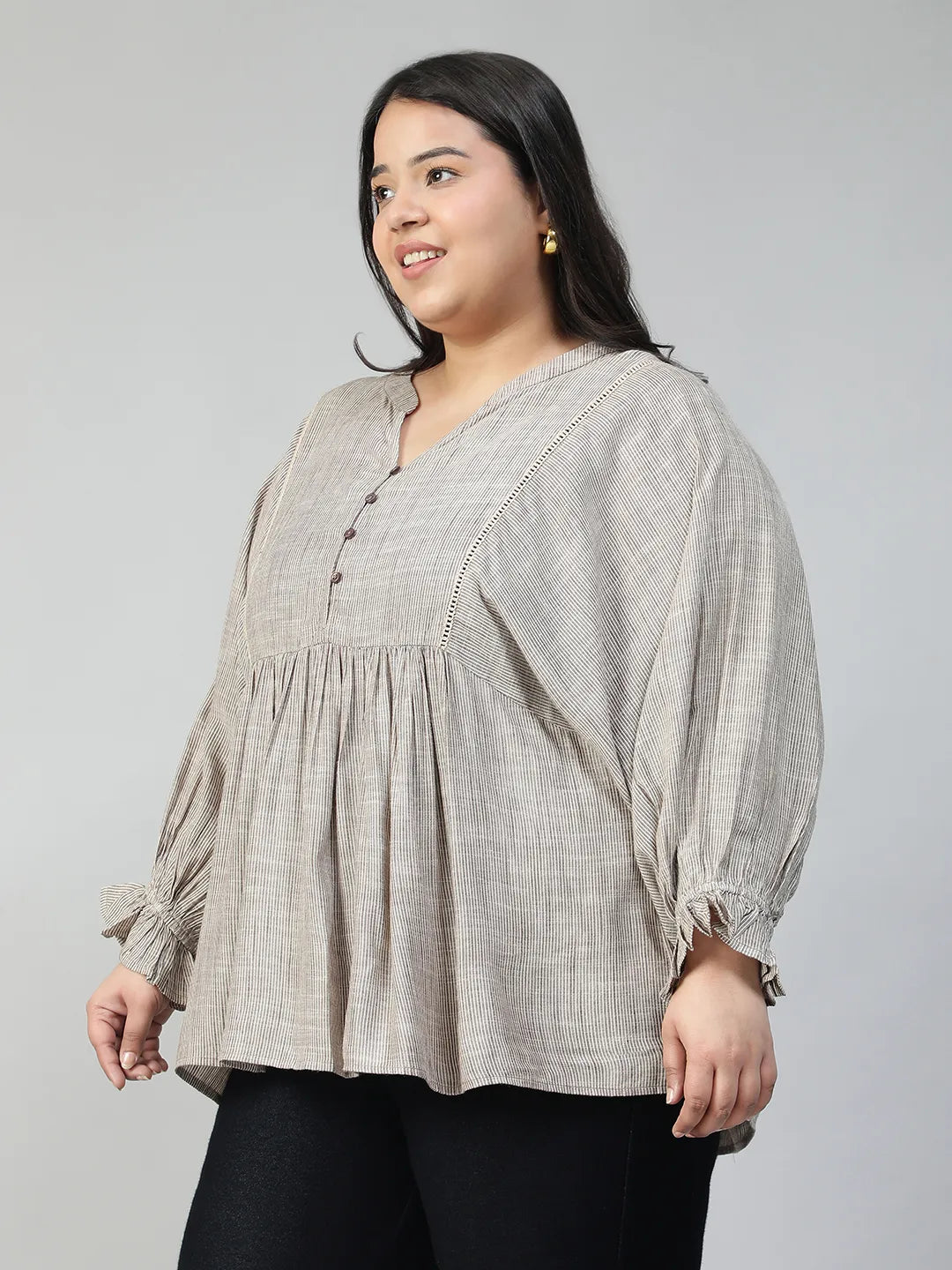 A woman with long dark hair is smiling and wearing a gray blouse with puffed sleeves.