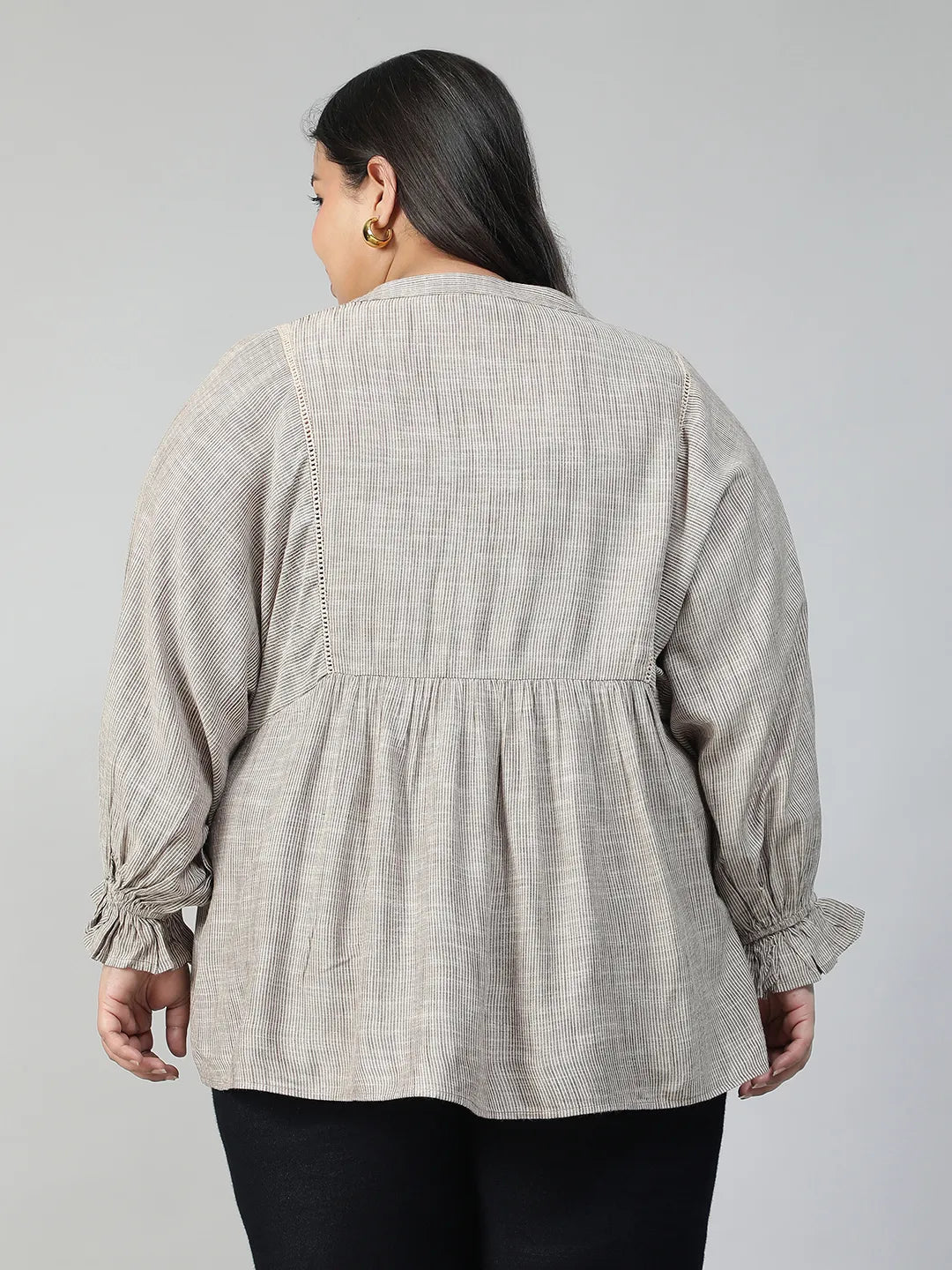 A woman with long dark hair is smiling and wearing a gray blouse with puffed sleeves.
