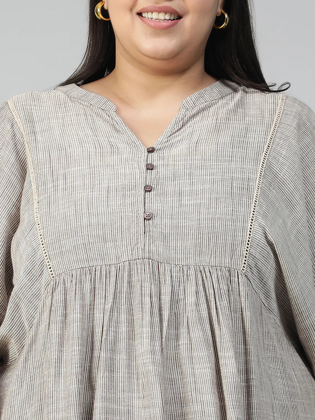 A woman with long dark hair is smiling and wearing a gray blouse with puffed sleeves.