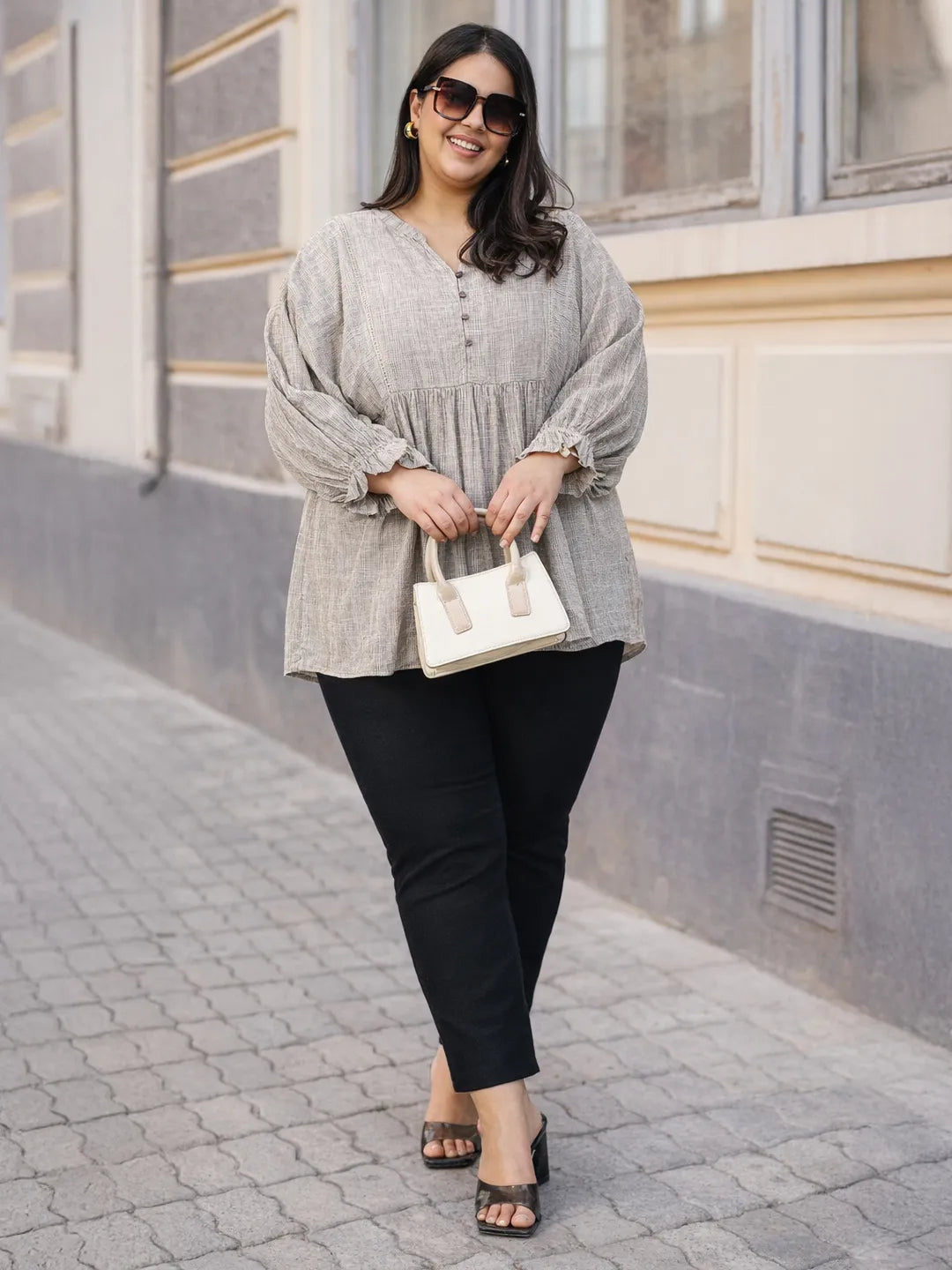 A woman with long dark hair is smiling and wearing a gray blouse with puffed sleeves.