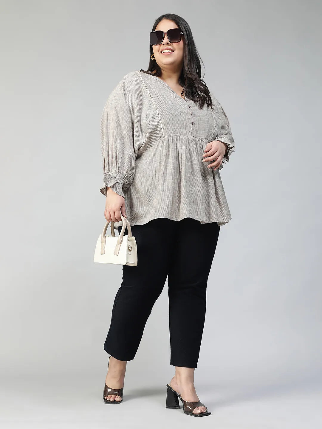 A woman with long dark hair is smiling and wearing a gray blouse with puffed sleeves.