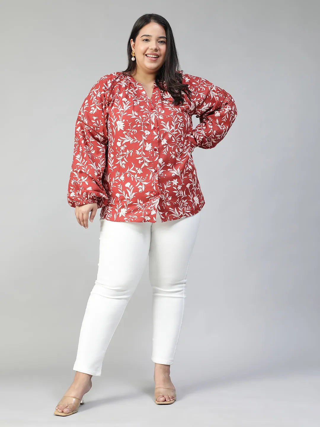 A woman wearing a red and white floral blouse with long sleeves, smiling at the camera.