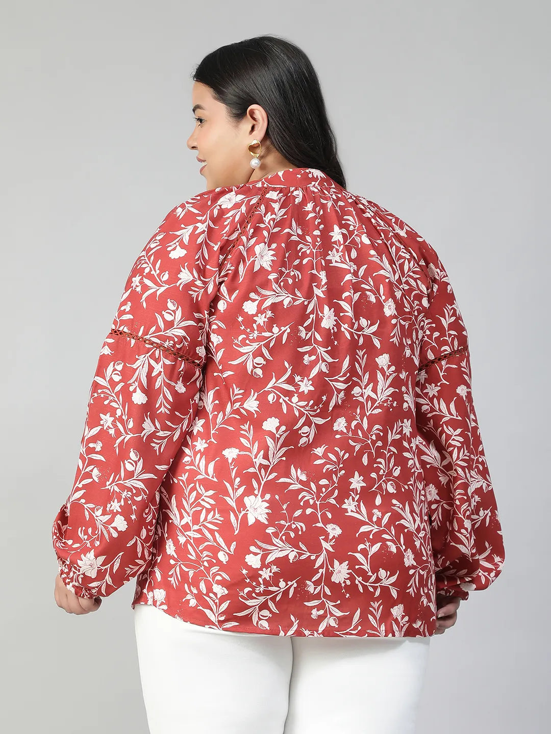 A woman wearing a red and white floral blouse with long sleeves, smiling at the camera.