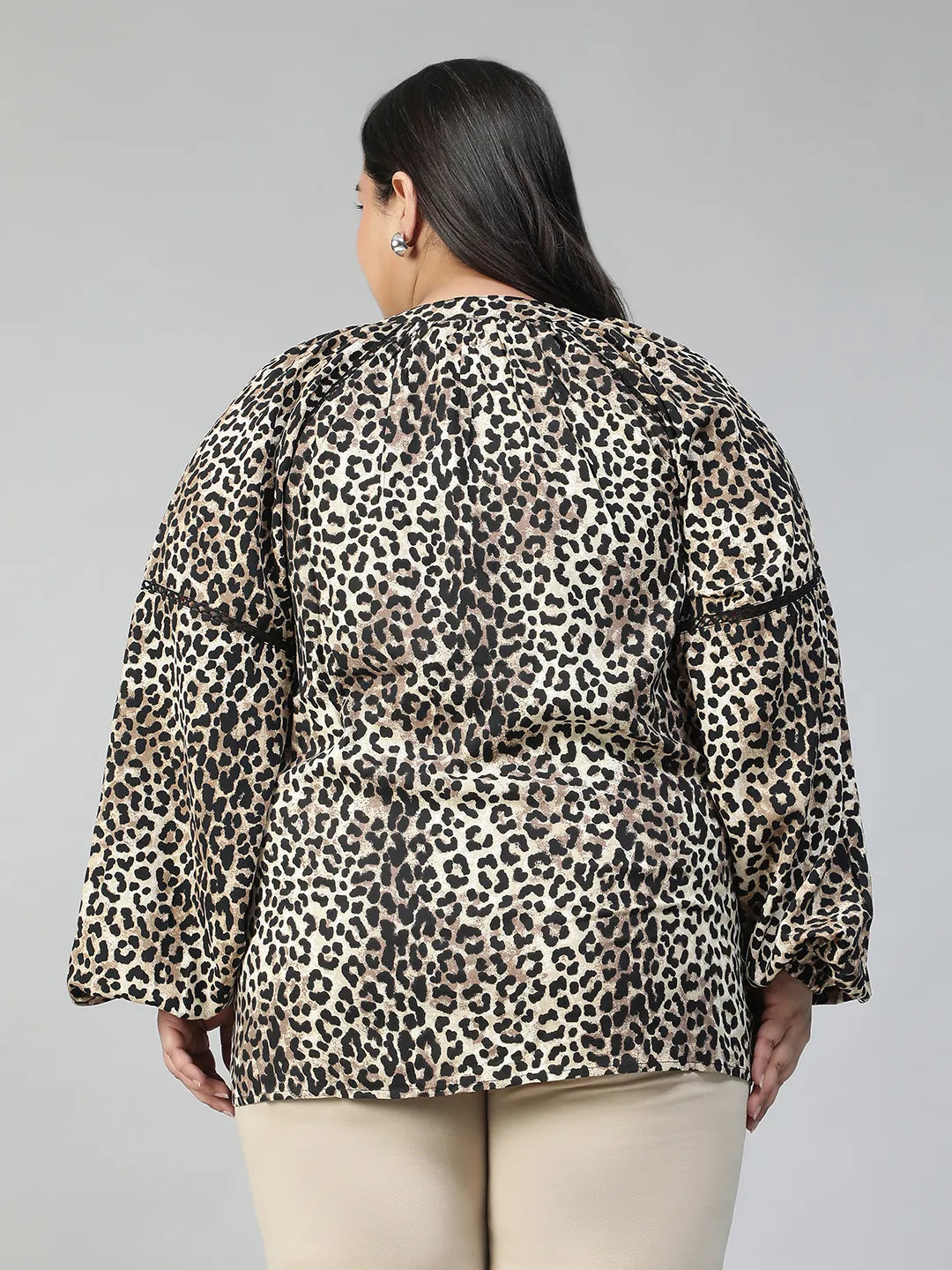 A smiling woman wearing a leopard print blouse with long sleeves.