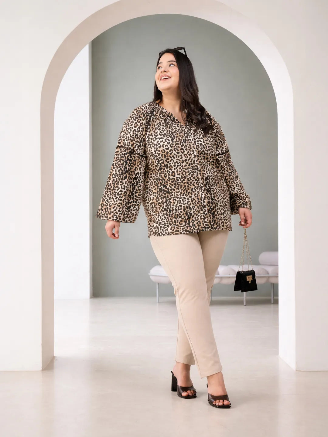 A smiling woman wearing a leopard print blouse with long sleeves.
