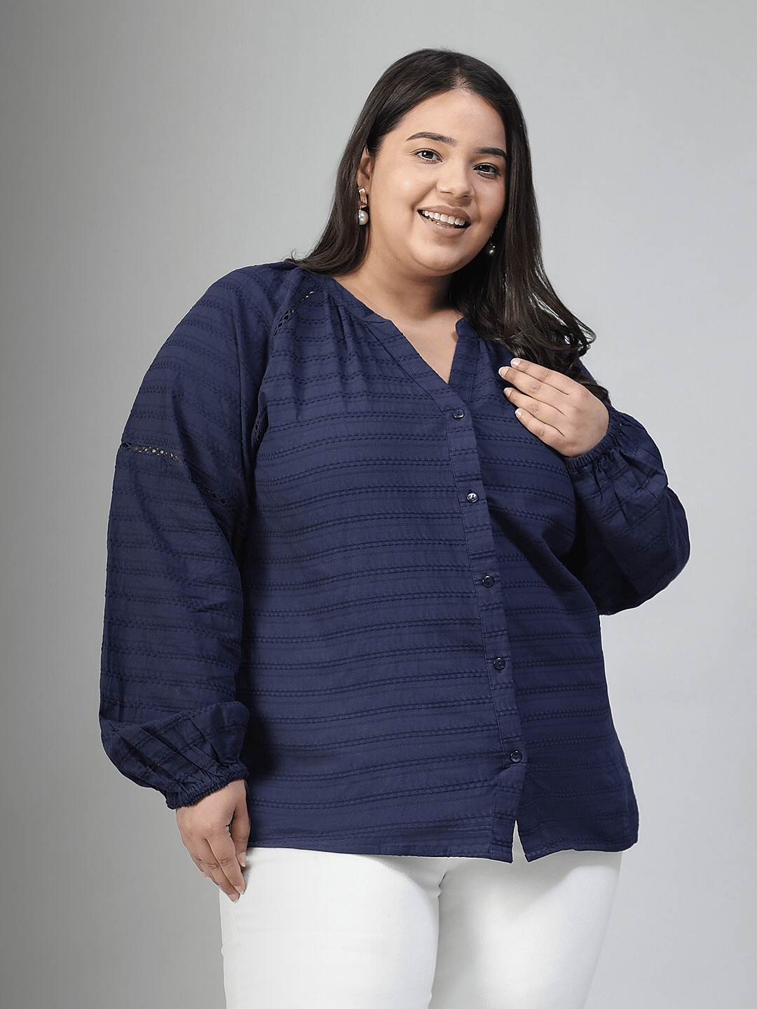 A woman with long dark hair is smiling and wearing a navy blue blouse with a v-neck and button-down sleeves.
