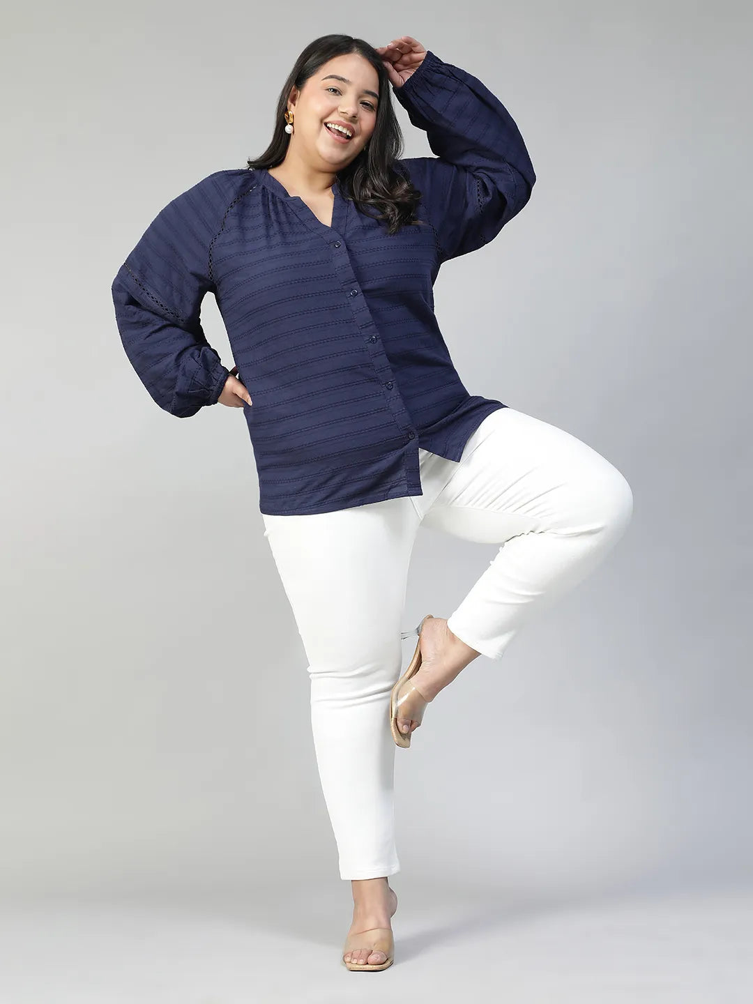 A woman with long dark hair is smiling and wearing a navy blue blouse with a v-neck and button-down sleeves.