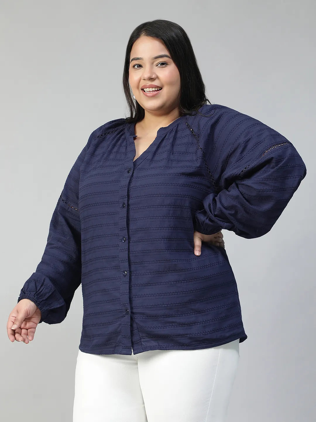 A woman with long dark hair is smiling and wearing a navy blue blouse with a v-neck and button-down sleeves.