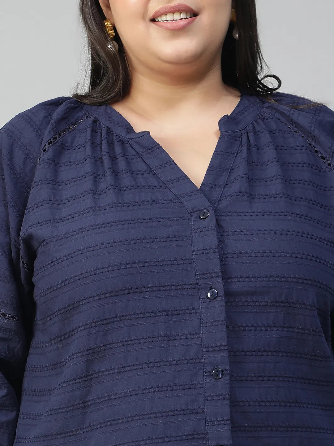 A woman with long dark hair is smiling and wearing a navy blue blouse with a v-neck and button-down sleeves.