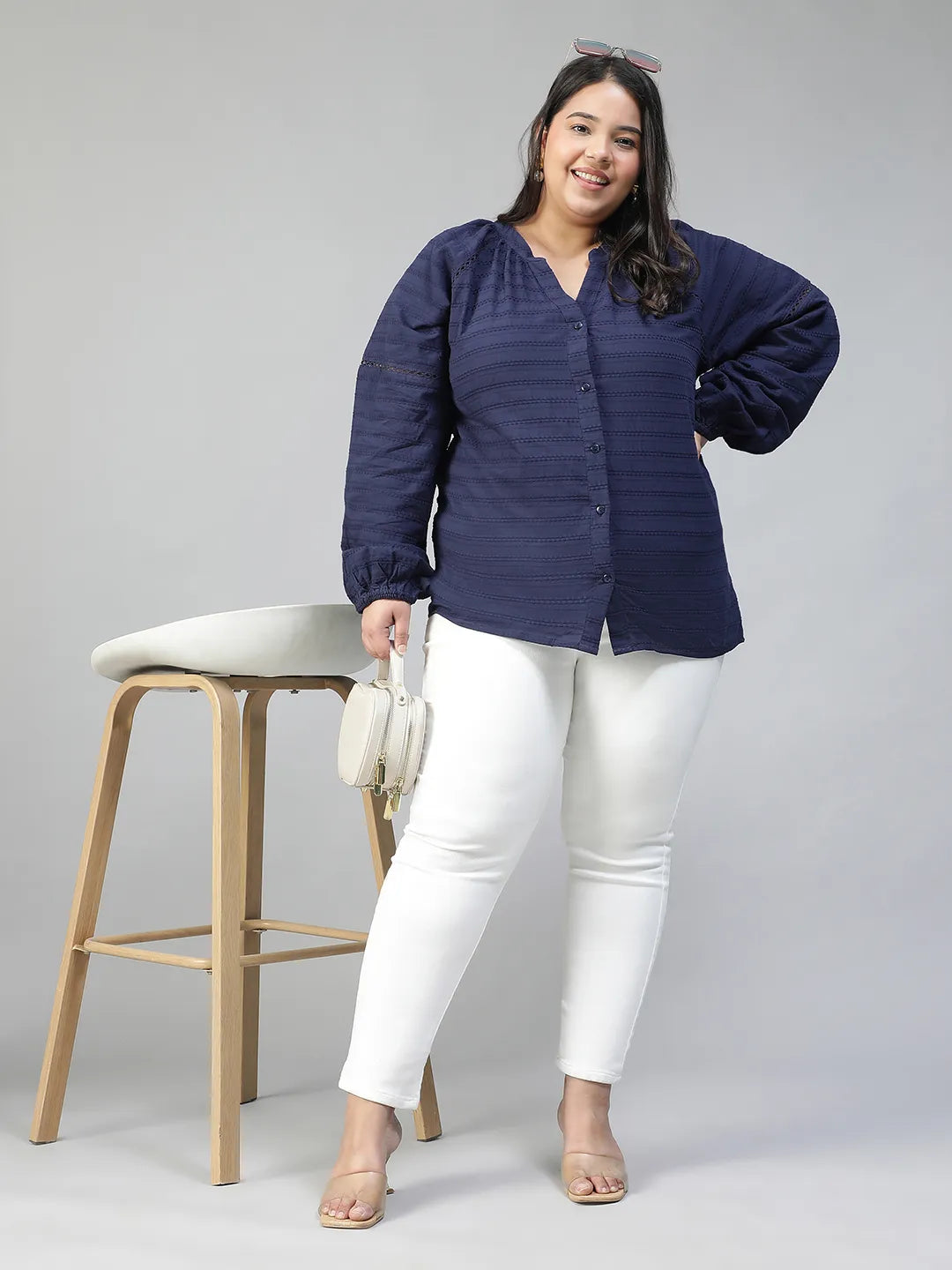 A woman with long dark hair is smiling and wearing a navy blue blouse with a v-neck and button-down sleeves.