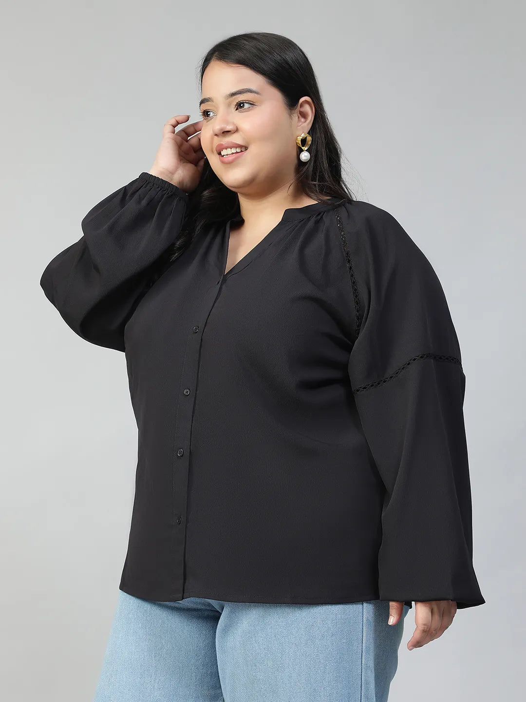 A woman with long dark hair is smiling and posing for the camera. She is wearing a black blouse with long sleeves and blue jeans.
