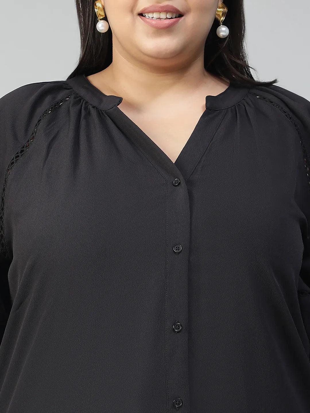A woman with long dark hair is smiling and posing for the camera. She is wearing a black blouse with long sleeves and blue jeans.