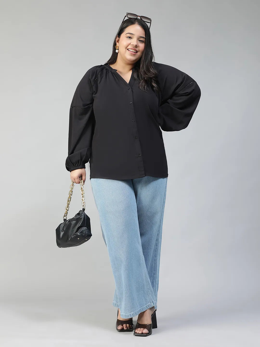 A woman with long dark hair is smiling and posing for the camera. She is wearing a black blouse with long sleeves and blue jeans.