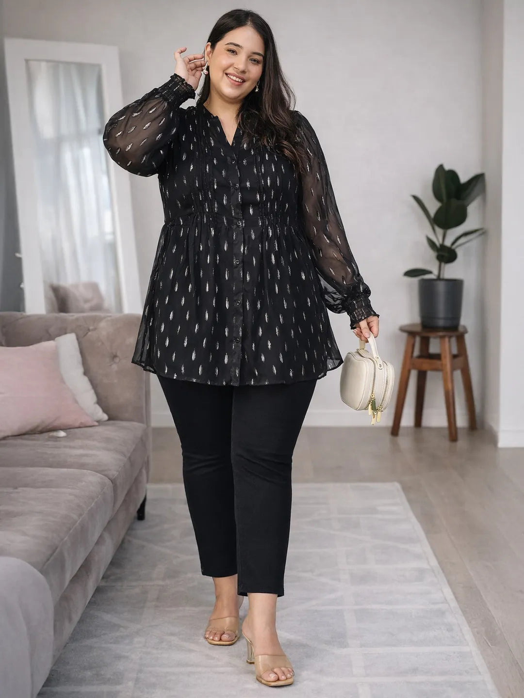A woman with long dark hair is smiling and posing for the camera. She is wearing a black blouse with silver dots and has her hand on her hip.