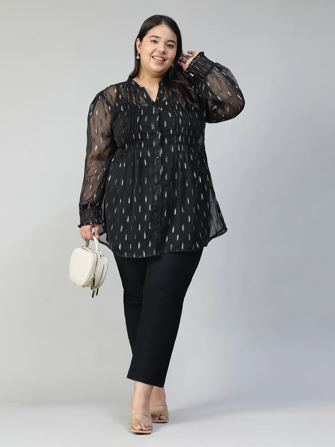 A woman with long dark hair is smiling and posing for the camera. She is wearing a black blouse with silver dots and has her hand on her hip.