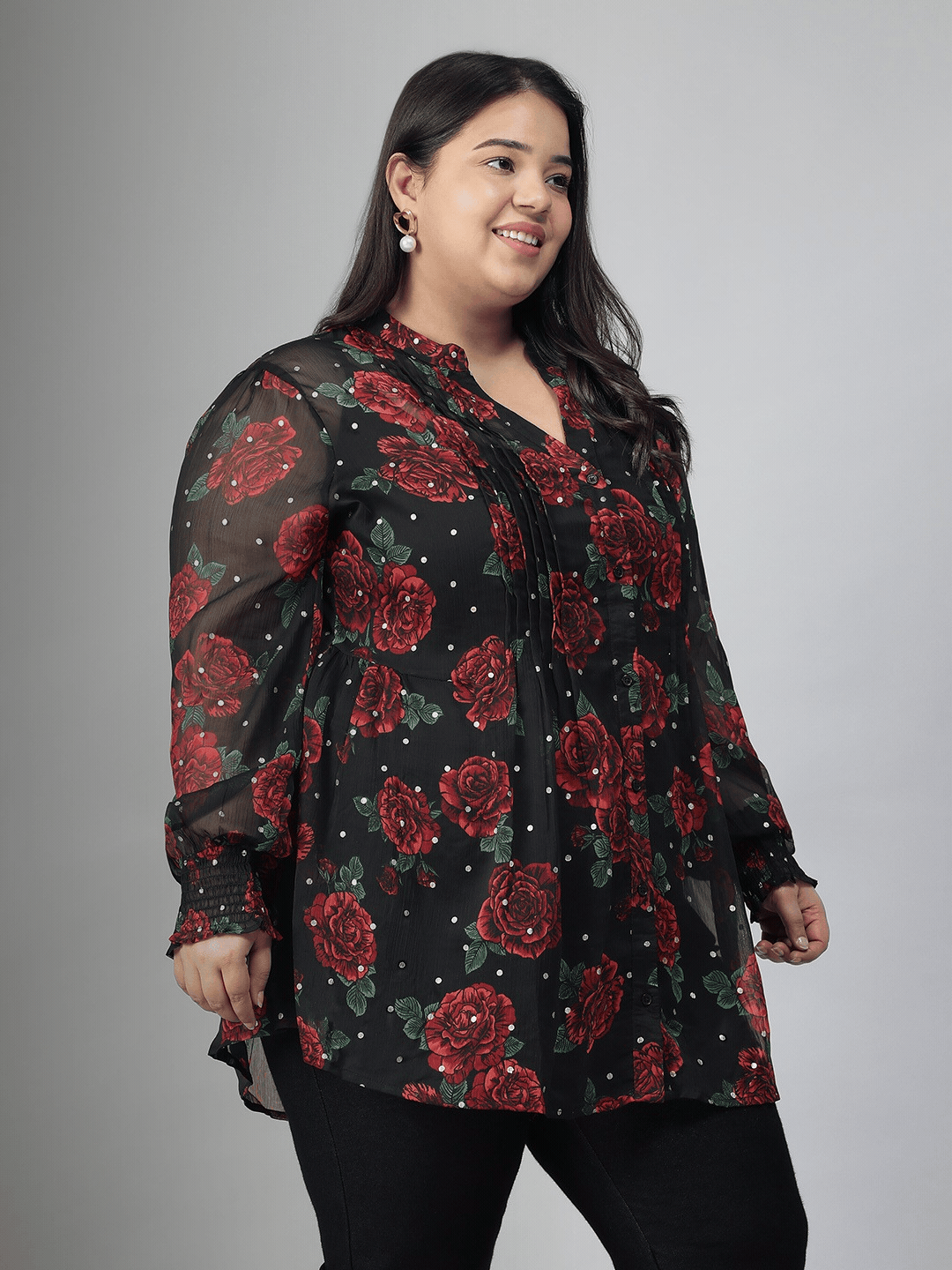 A woman wearing a black and red floral blouse with a high collar and puffed sleeves, smiling at the camera.