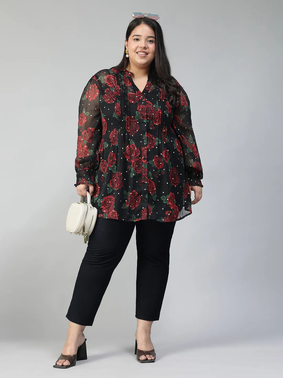 A woman wearing a black and red floral blouse with a high collar and puffed sleeves, smiling at the camera.