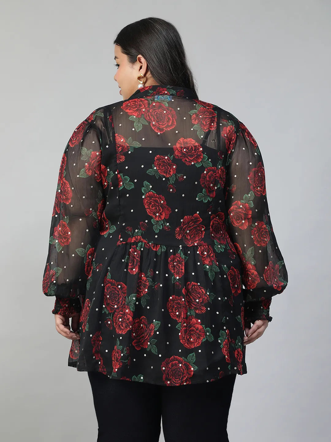 A woman wearing a black and red floral blouse with a high collar and puffed sleeves, smiling at the camera.