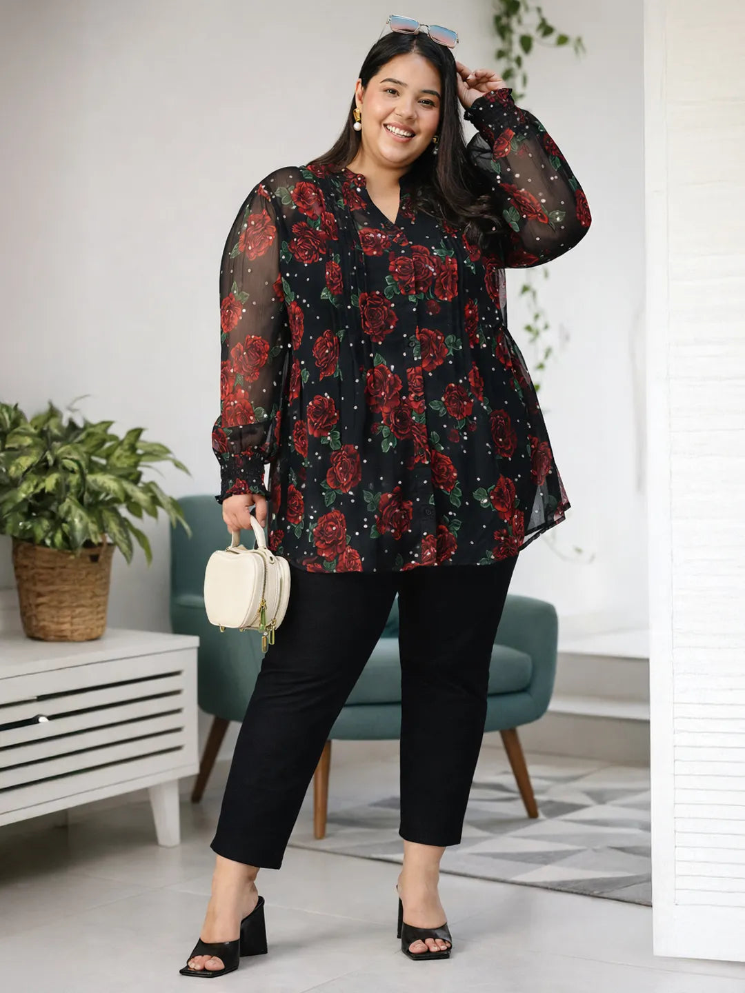 A woman wearing a black and red floral blouse with a high collar and puffed sleeves, smiling at the camera.