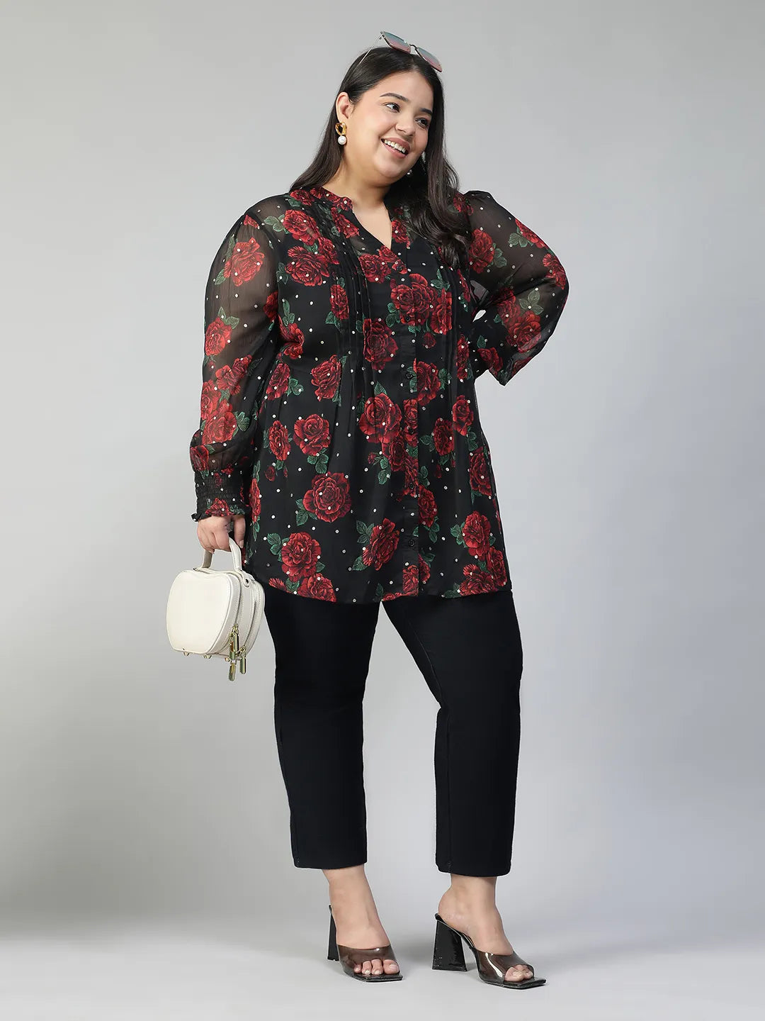 A woman wearing a black and red floral blouse with a high collar and puffed sleeves, smiling at the camera.