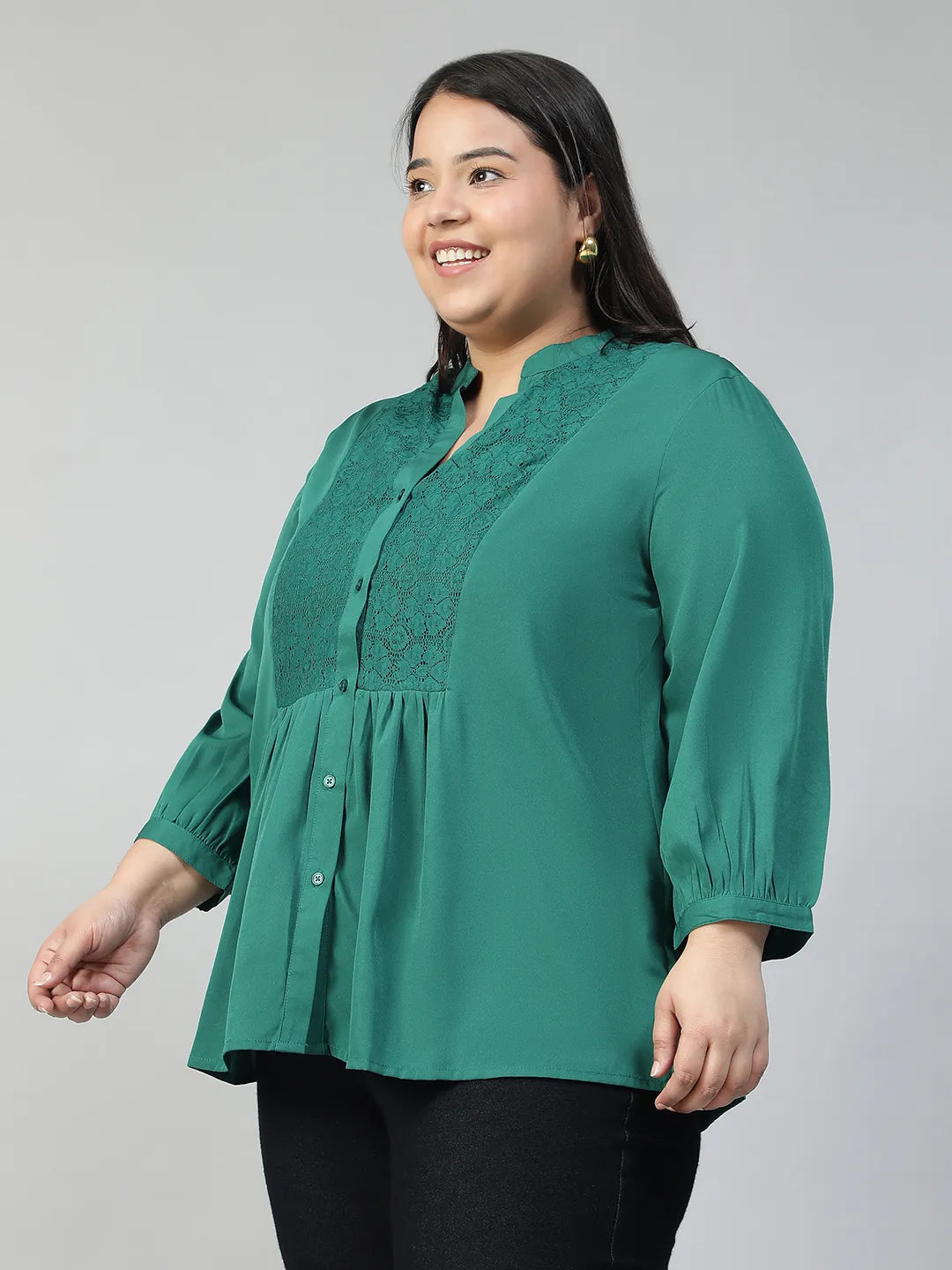 A smiling woman wearing a green blouse with lace detailing and puffed sleeves, posing confidently with her hand on her hip.