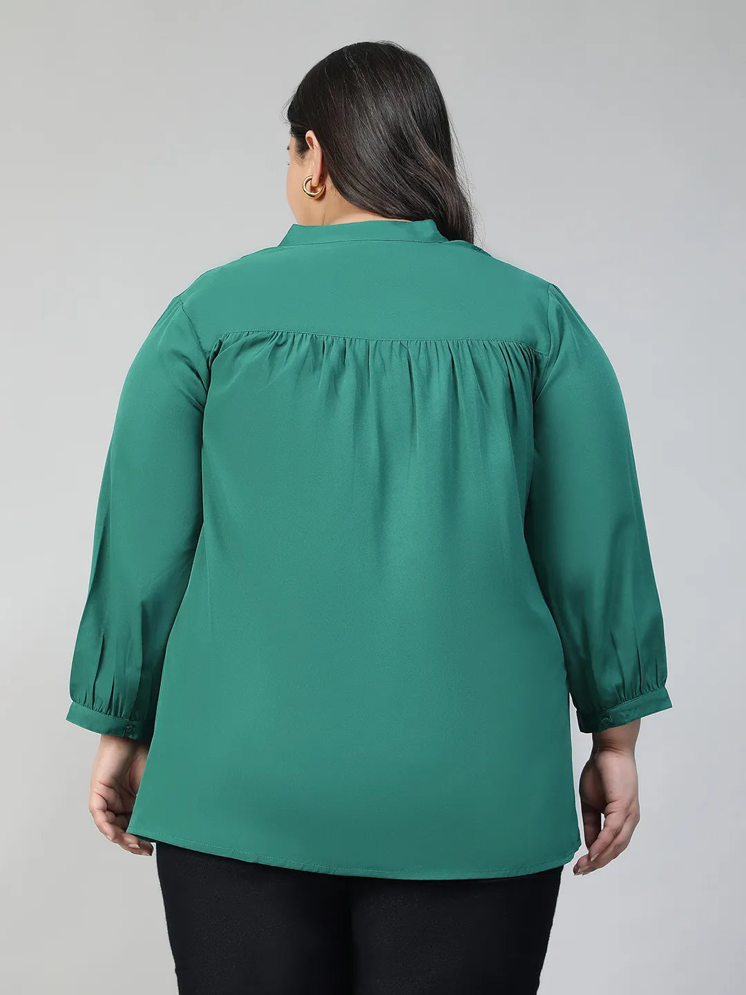 A smiling woman wearing a green blouse with lace detailing and puffed sleeves, posing confidently with her hand on her hip.