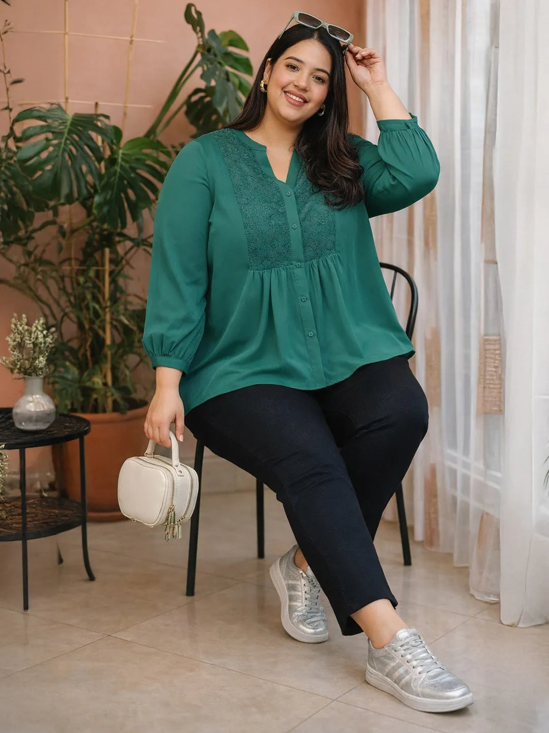 A smiling woman wearing a green blouse with lace detailing and puffed sleeves, posing confidently with her hand on her hip.