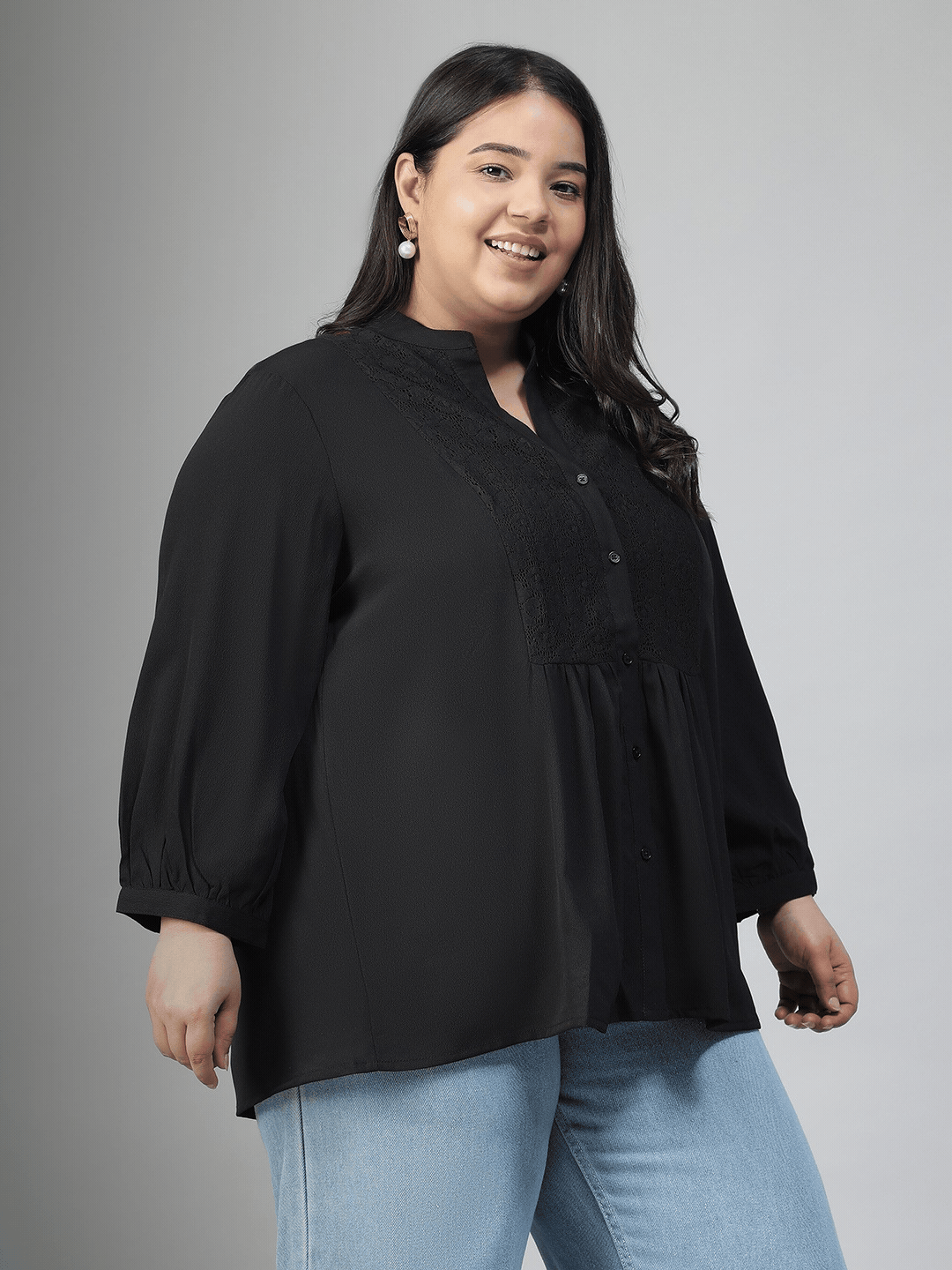A woman with long dark hair is smiling and posing for the camera, wearing a black blouse with lace detailing and puffed sleeves.