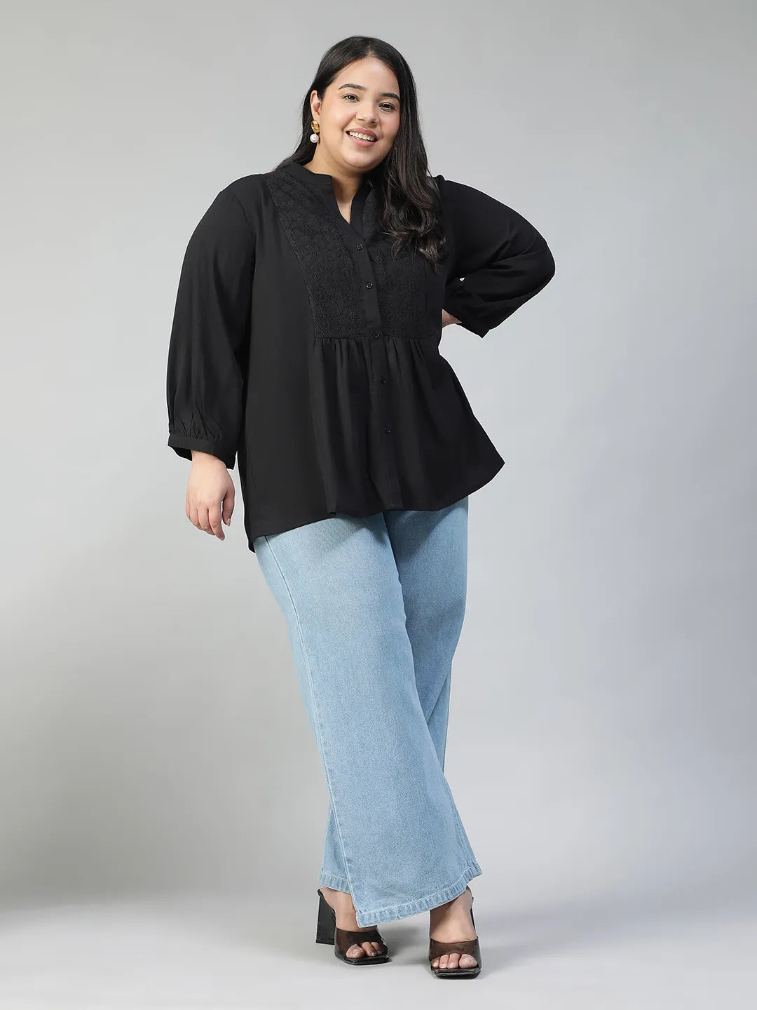A woman with long dark hair is smiling and posing for the camera, wearing a black blouse with lace detailing and puffed sleeves.