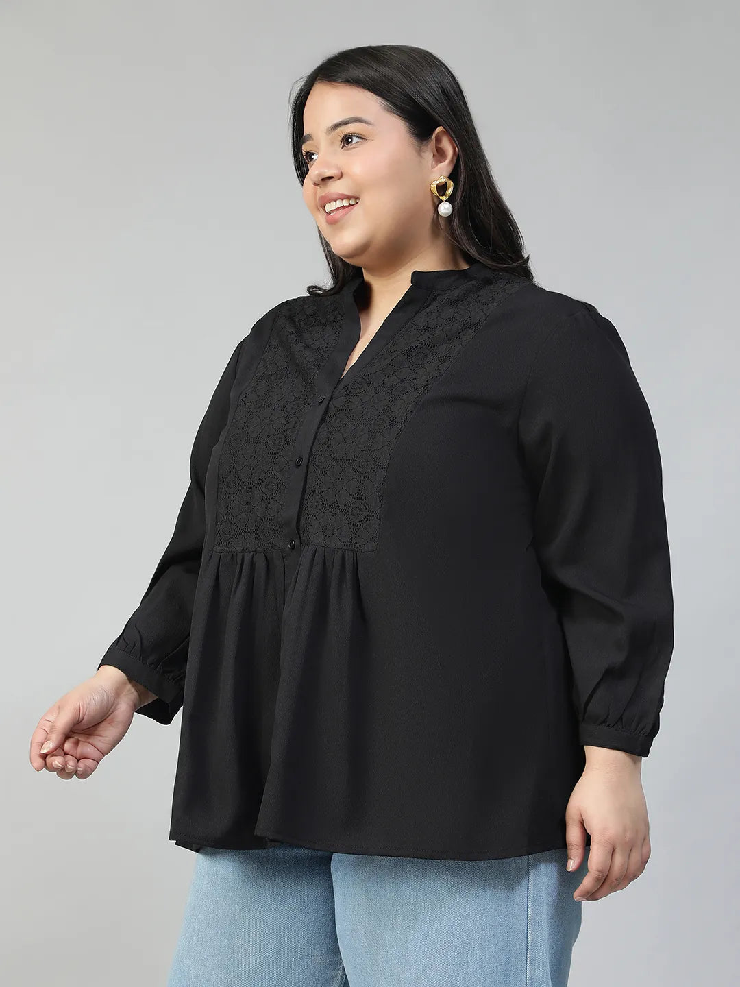 A woman with long dark hair is smiling and posing for the camera, wearing a black blouse with lace detailing and puffed sleeves.
