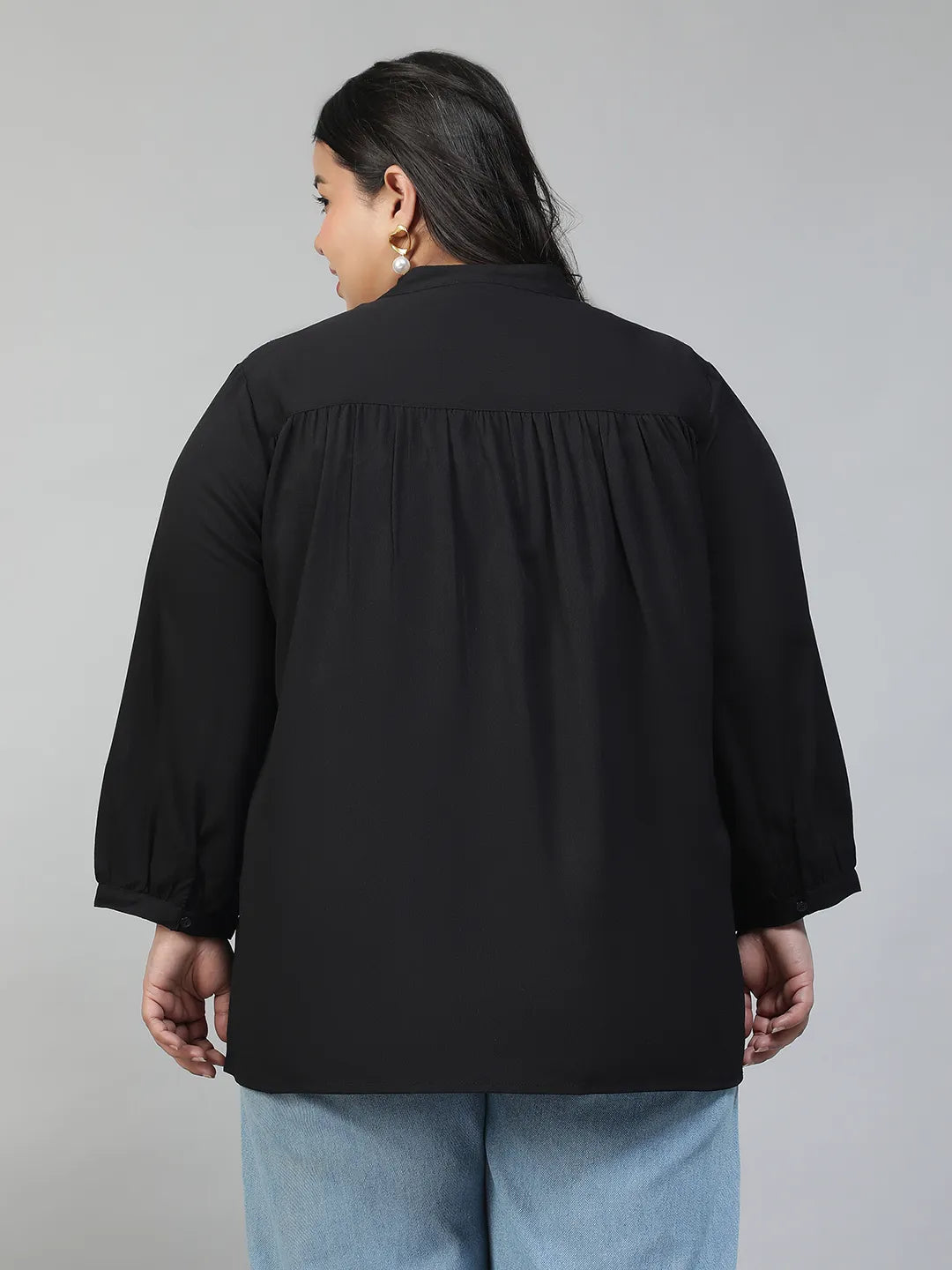 A woman with long dark hair is smiling and posing for the camera, wearing a black blouse with lace detailing and puffed sleeves.