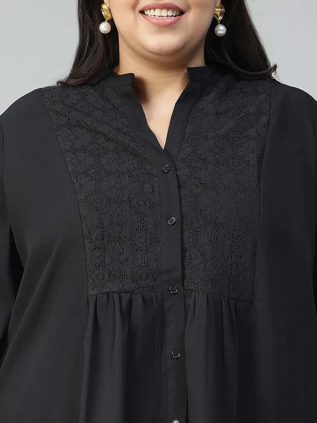 A woman with long dark hair is smiling and posing for the camera, wearing a black blouse with lace detailing and puffed sleeves.